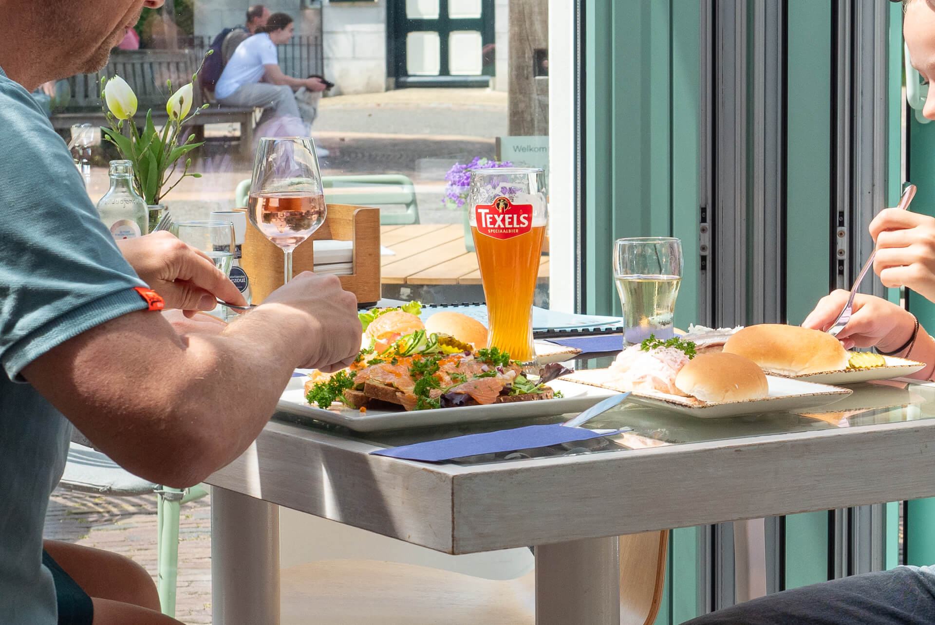 Twee gasten eten broodjes vis aan een tafel bij het open raam