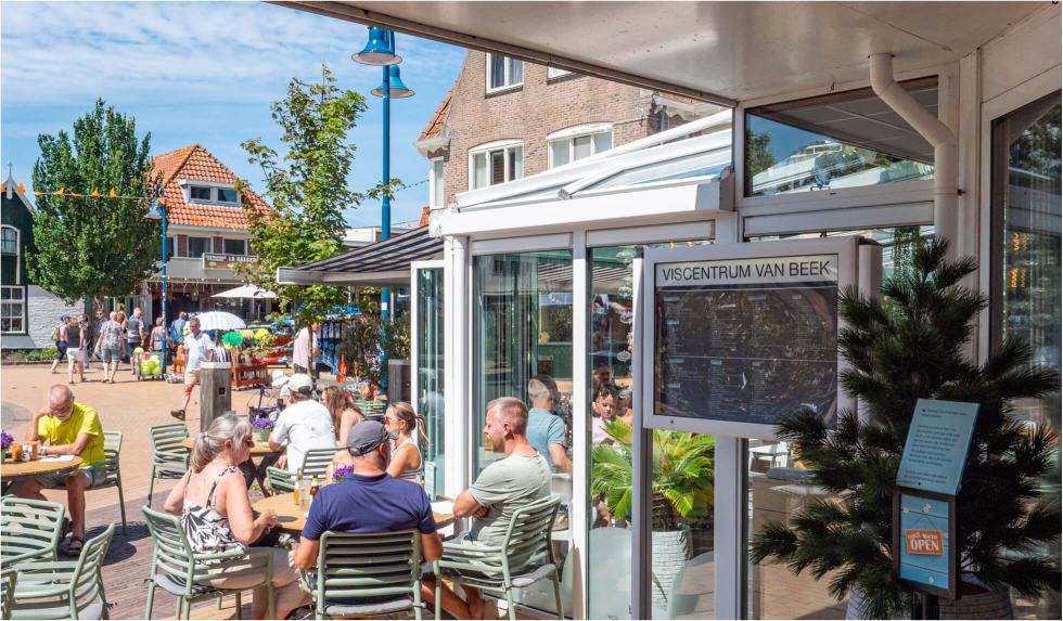 Terras op het dorpsplein in De Koog, met gasten aan tafel bij de ingang van Viscentrum van Beek