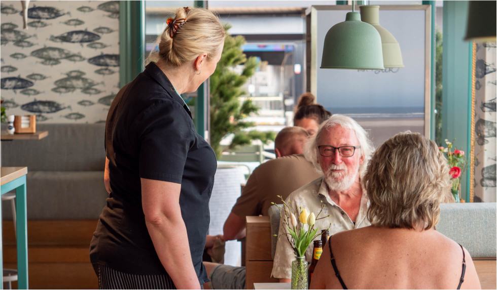 Medewerkster neemt de bestelling op bij twee gasten aan een tafel in het restaurant