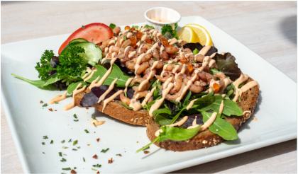 Broodje met Hollandse garnalen, sla en een dressing op een wit bord