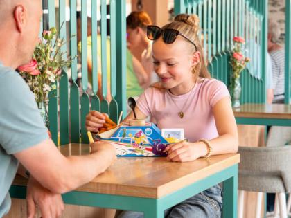 Meisje aan tafel met een kindermenu in een bootje, tegenover haar vader