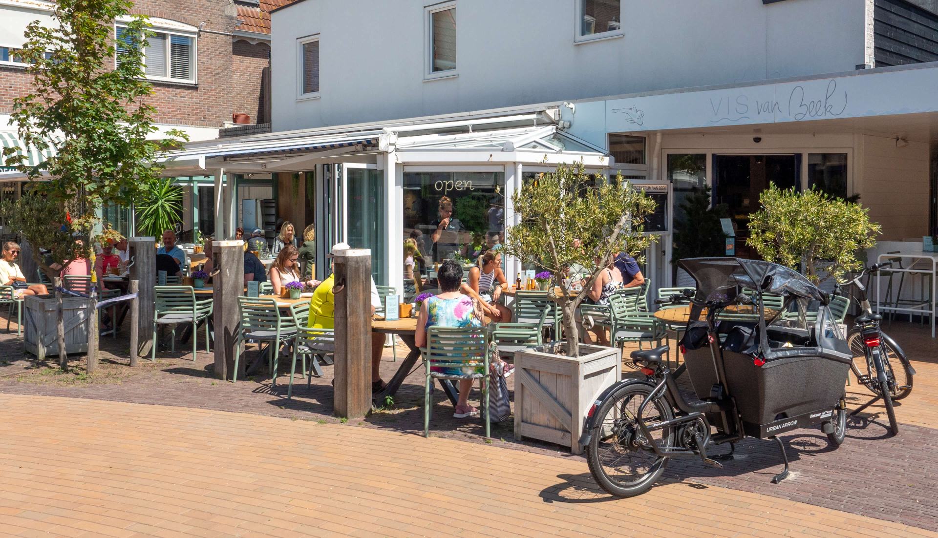 De gevel van Vis van Beek aan het dorpsplein in De Koog, met gasten op het terras in de zon